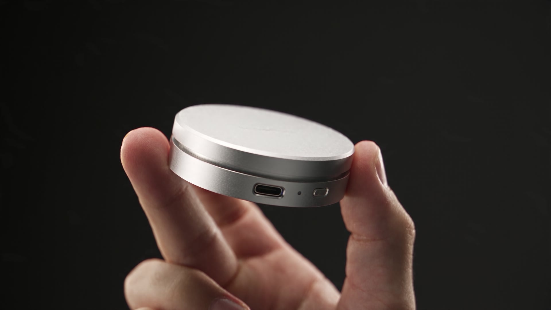 ScalePod held between a thumb and forefinger, showing its slim aluminum profile, USB-C port and power button.
